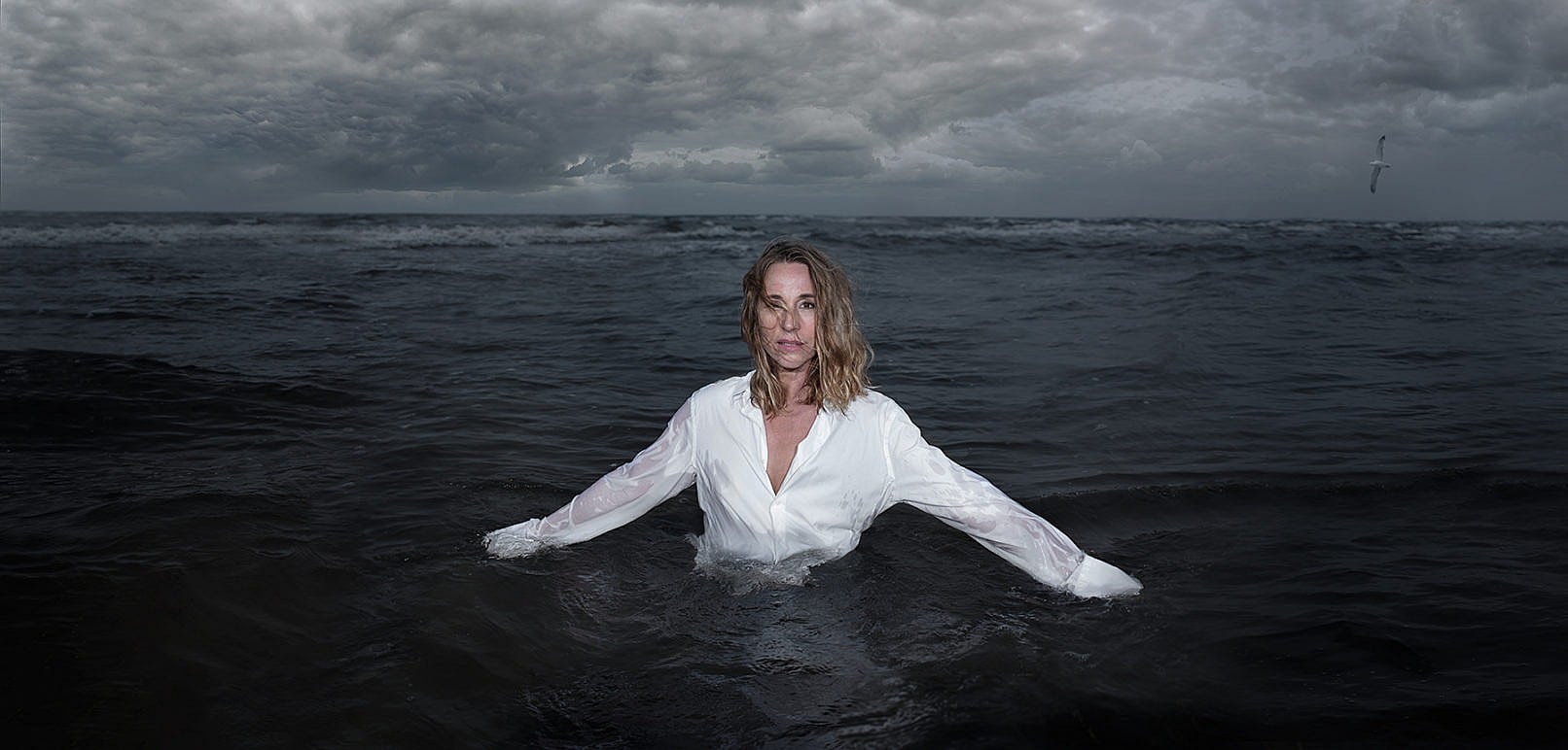 Ann-Eleonora Jørgensen, står i hvid skjorte i vandet, på en kold efterårsdag. Fotograf Christian Krog - Portrætfotograf