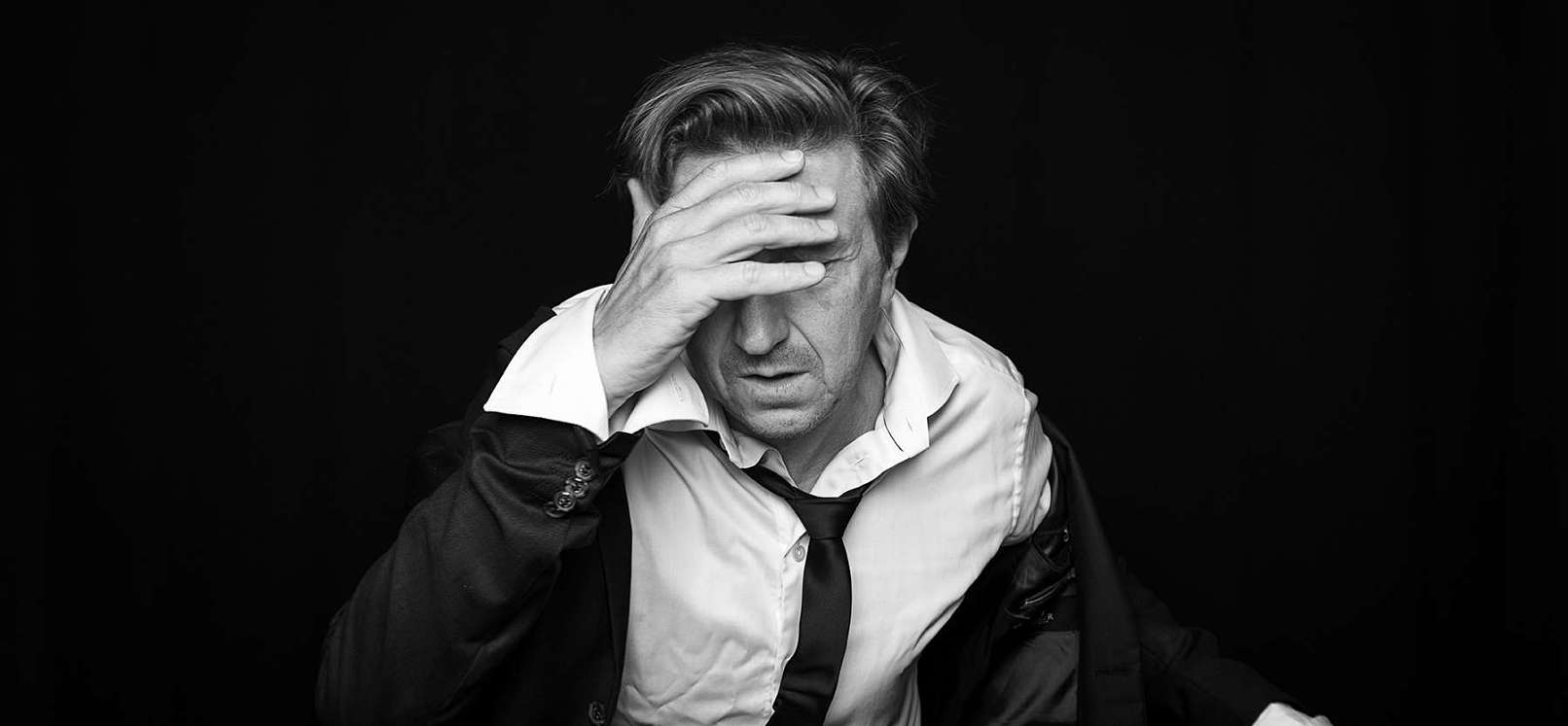 Nicolaj sidder ved et bord , tager sig til hovedet, lit opgivende. Billedet er taget af Portrætfptogtaf Christian Krog. Nicolaj Kopernikus. Forbrydelsen. Klassefesten